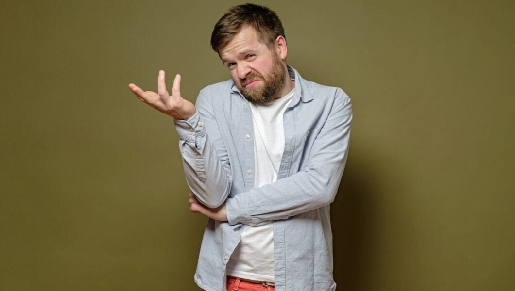 Caucasian man with a doubtful expression on face shrugs, makes a hand gesture and uncertain grimace